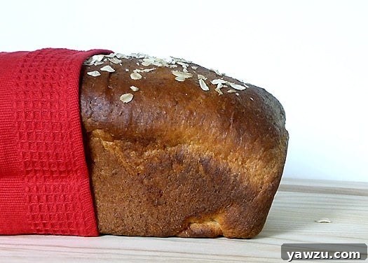 Side view of a perfectly baked loaf of honey oatmeal sandwich bread, showcasing its golden crust and wholesome texture.