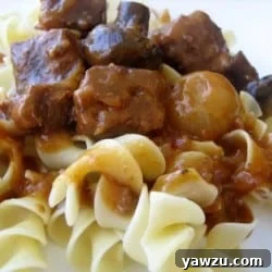 Close-up of a serving of Slow Cooker Beef Burgundy with egg noodles, showing tender beef cubes, glazed pearl onions, and mushrooms.