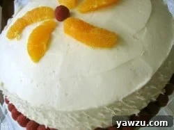 Beautifully frosted layer cake garnished with raspberries and orange slices, ready for a party.
