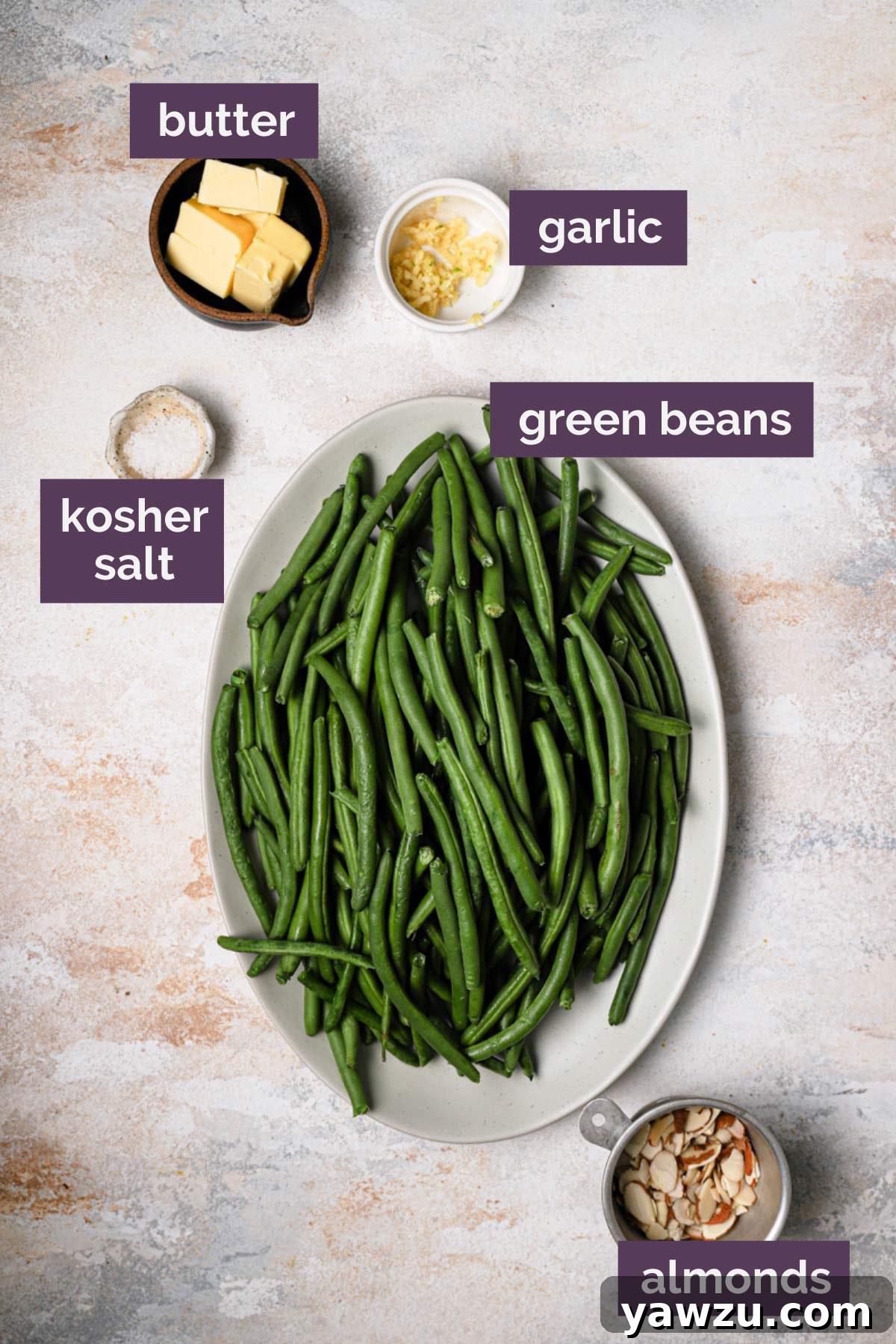 Fresh green beans, sliced almonds, unsalted butter, and minced garlic prepped and arranged on a white cutting board, labeled for convenience.
