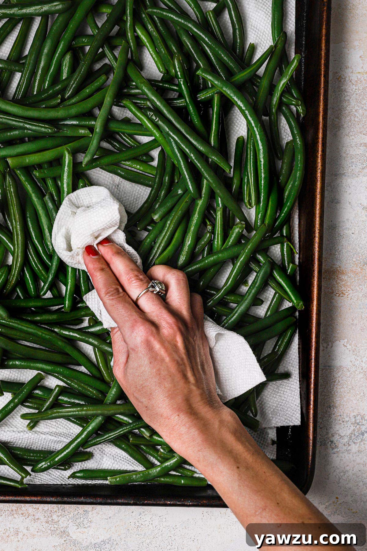 Blanched green beans draining on a baking sheet lined with paper towels, ensuring they are thoroughly dry.