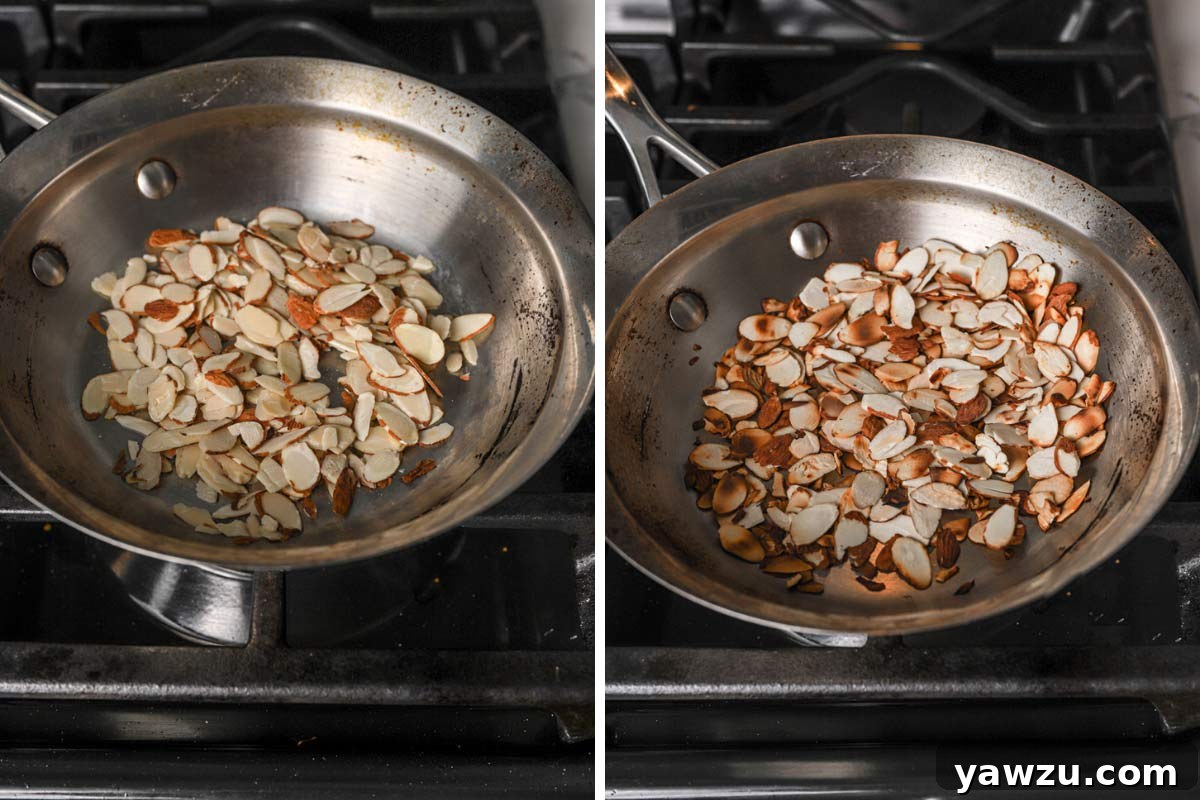 Sliced almonds being evenly toasted in a gleaming stainless steel skillet over medium heat.