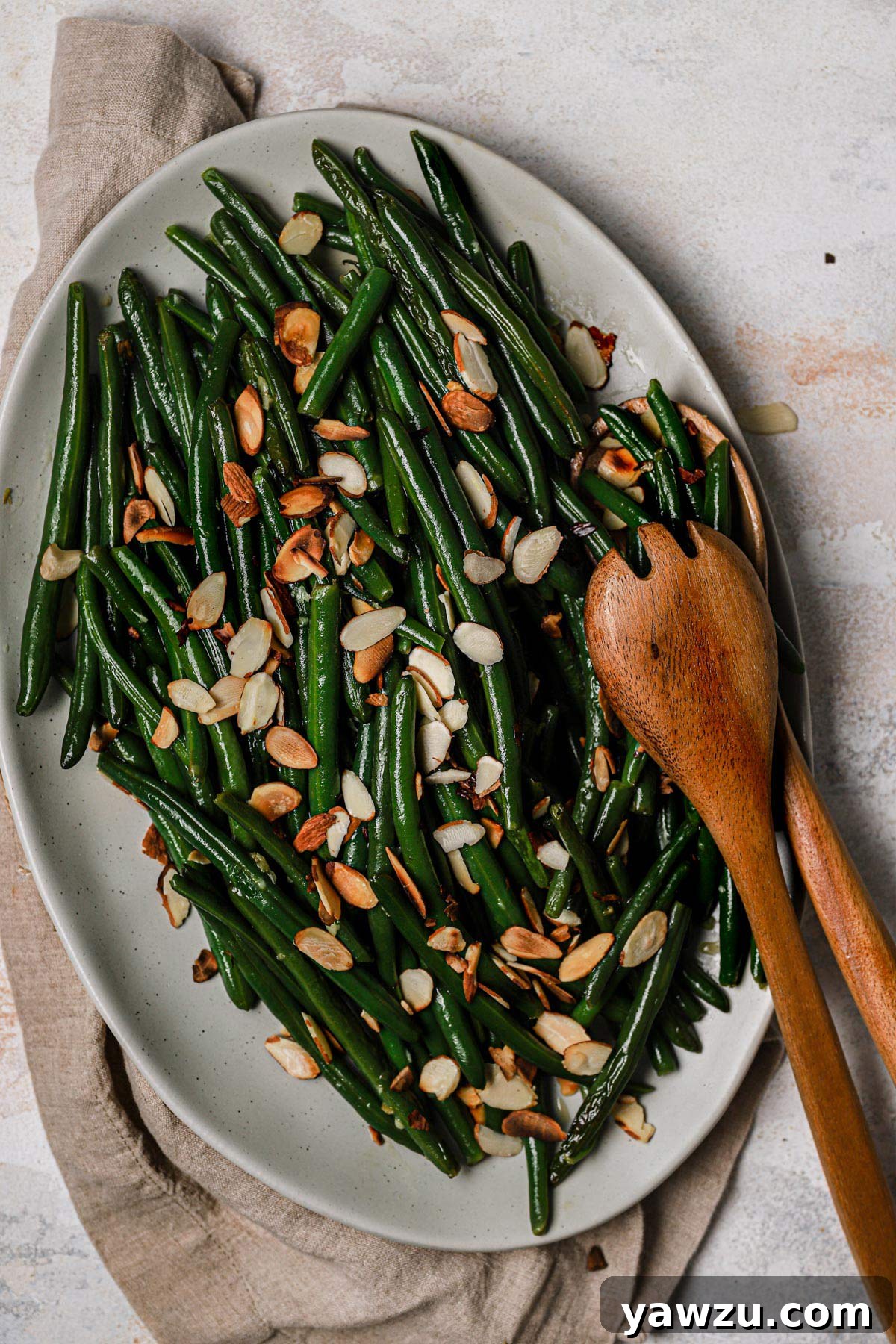 A close-up shot of Green Beans Almondine, perfectly tossed with toasted sliced almonds, in a decorative white serving dish, ready to be enjoyed.