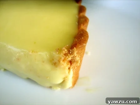 Close up image of a slice of orange cream tart on a white plate, revealing the creamy orange filling and the perfectly baked, flaky crust. A small segment of fresh orange garnish adds a pop of color.