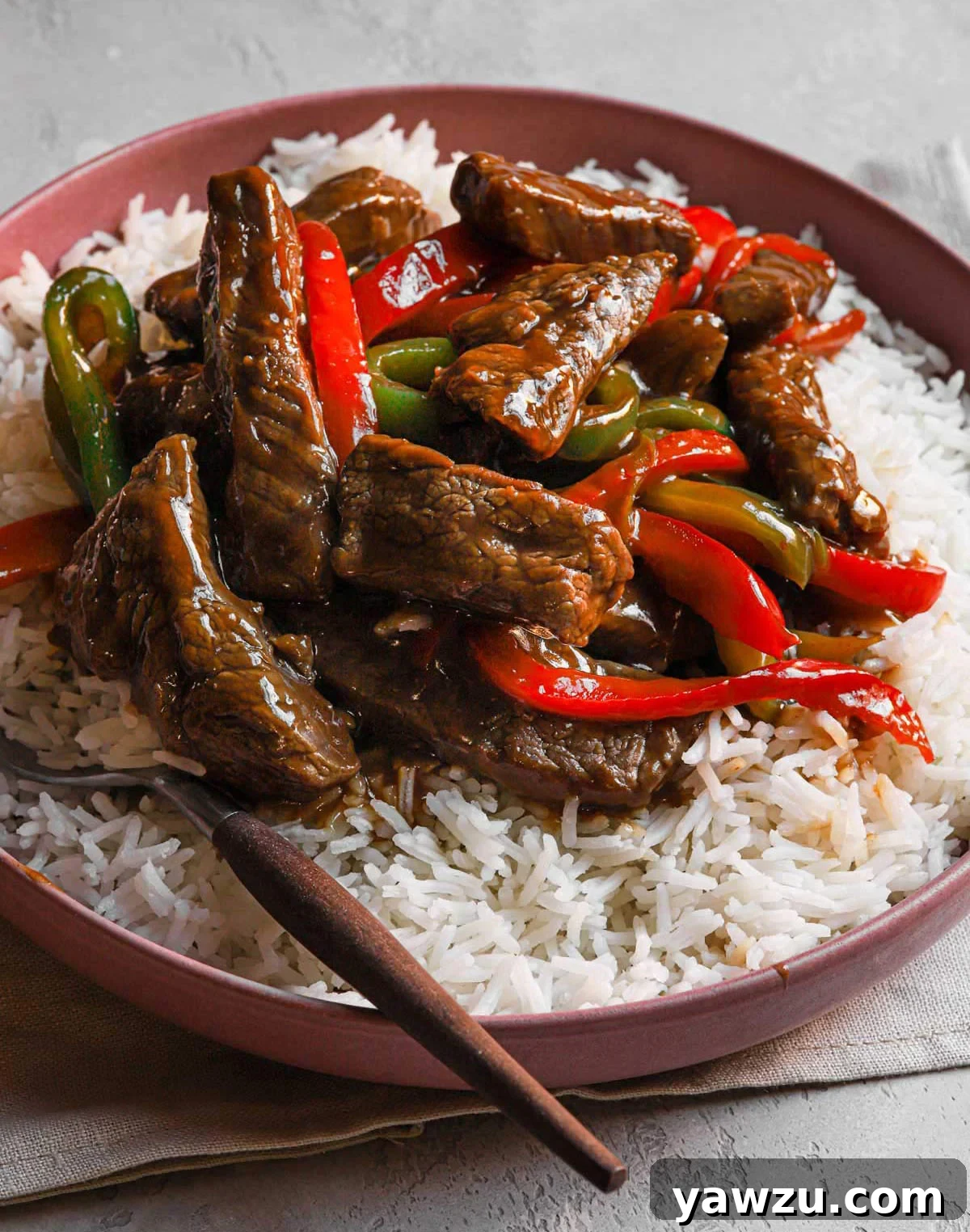 Delicious pepper steak stir fry served over white rice in a bowl, garnished with sesame seeds.