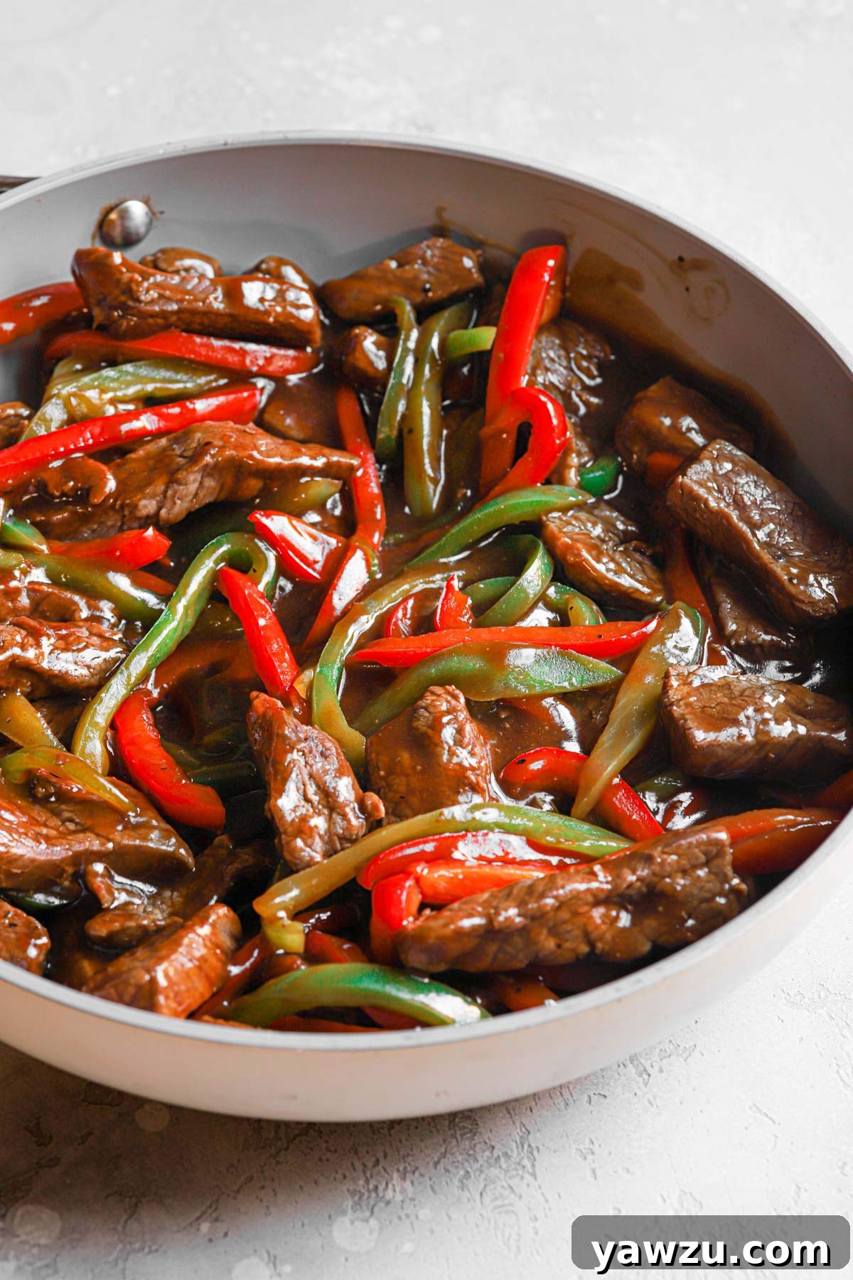 Close-up of pepper steak stir fry in a skillet, beautifully coated in the glossy, rich sauce.