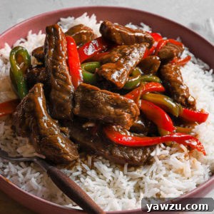 A serving of easy pepper steak stir fry in a white bowl with rice.