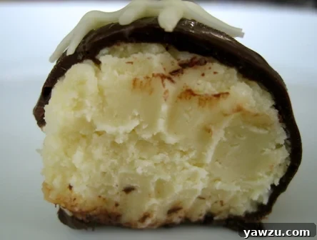 A perfectly halved cheesecake truffle revealing its dense, creamy cheesecake interior, encased in a smooth, dark chocolate coating.