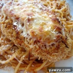 Chicken parmesan on top of noodles on a white plate.