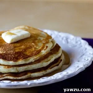 Stack of 3 pancakes topped with a pat of butter and maple syrup on a white plate.
