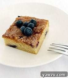 Square of blueberry butter cake topped with blueberries on a white plate with a fork.