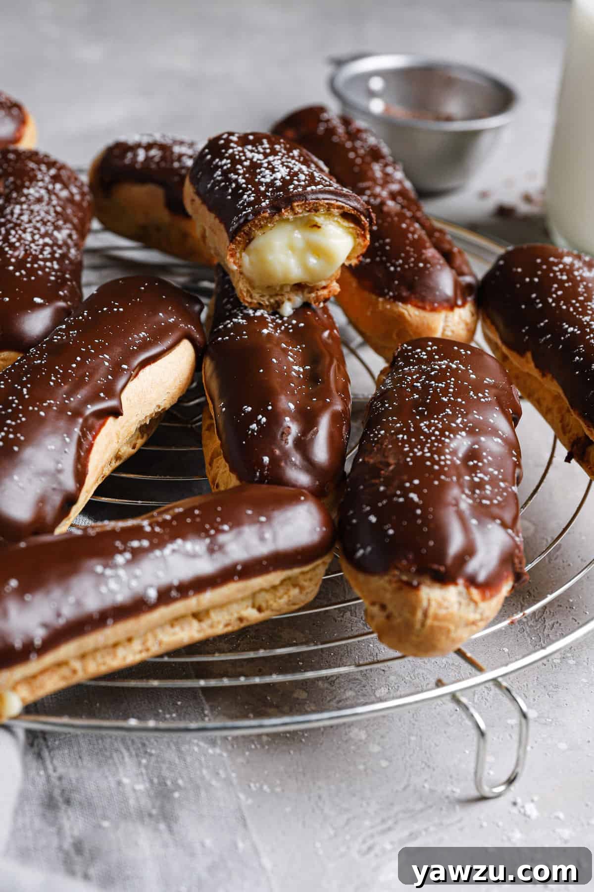 From the side, eclairs cooling on a wire rack with one eclair showing the inside of the pastry.