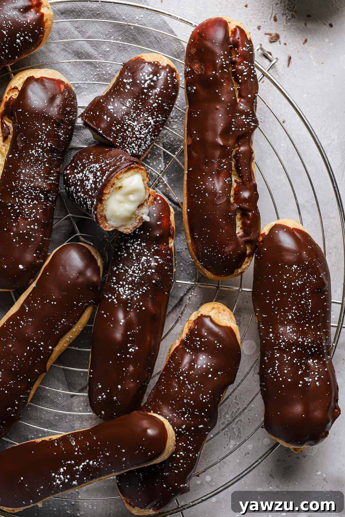 Chocolate dipped eclairs on a cooling rack with a bite taken out of the center eclair.