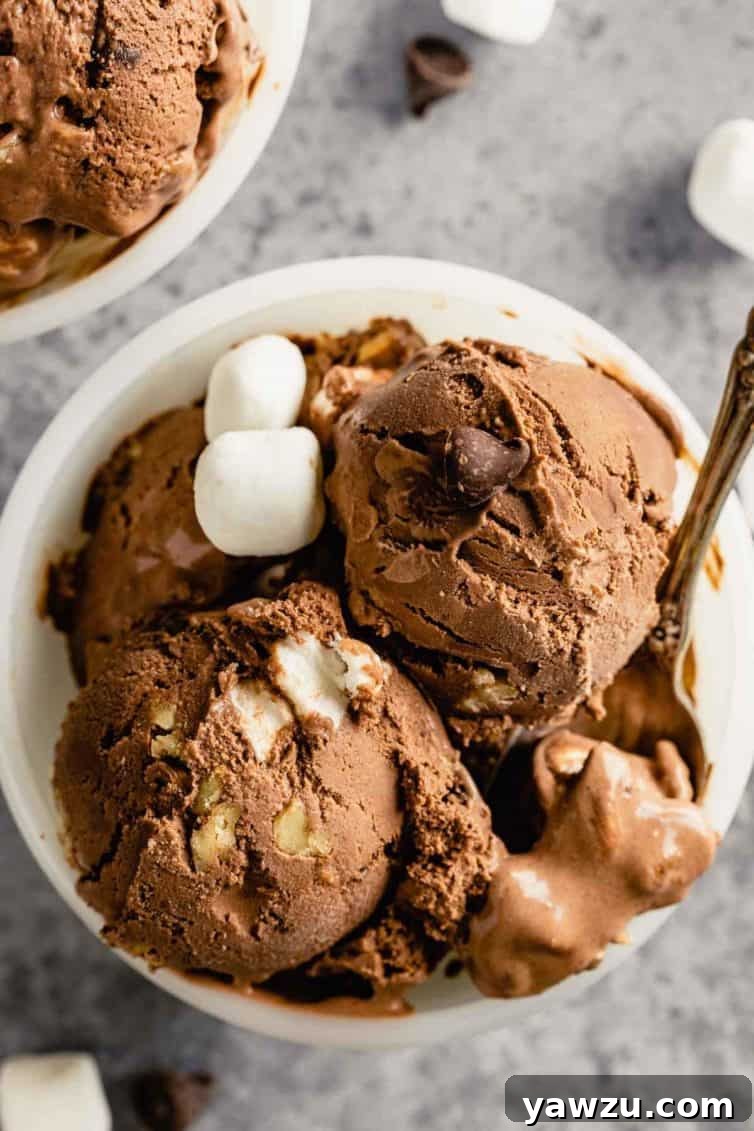 A pristine white bowl overflowing with homemade rocky road ice cream, accompanied by a spoon resting gracefully on the right side.