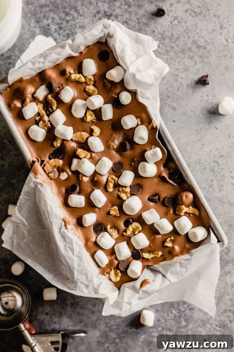 A vibrant top-down shot of rocky road ice cream neatly contained within a parchment paper-lined bread loaf pan, showcasing its rich texture and plentiful mix-ins.