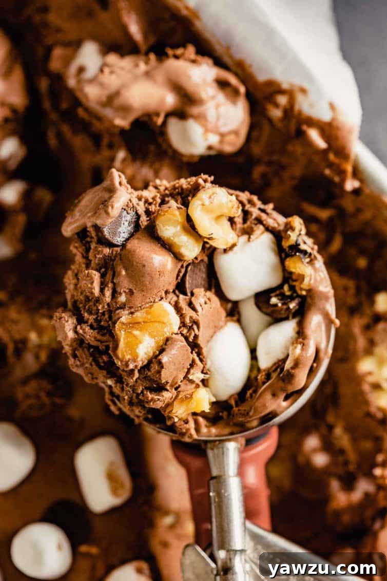 An ice cream scoop presenting a heaping, perfectly round scoop of rocky road ice cream, rich with visible mix-ins.