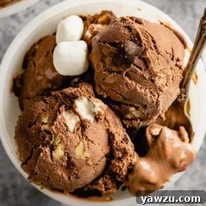 A white bowl with two scoops of rocky road ice cream on top, and a silver spoon resting on the right side of the bowl.