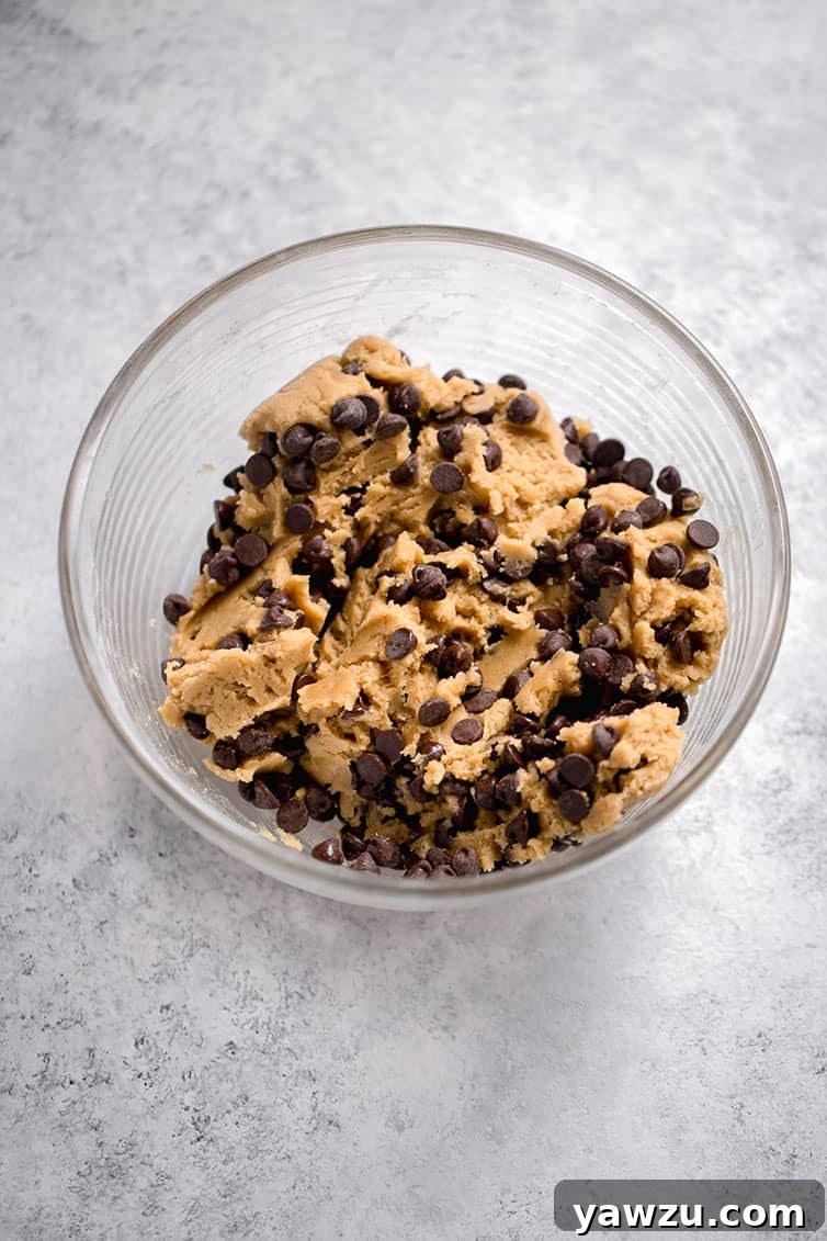 A close-up of thick chocolate chip cookie dough in a mixing bowl, showcasing its rich texture.