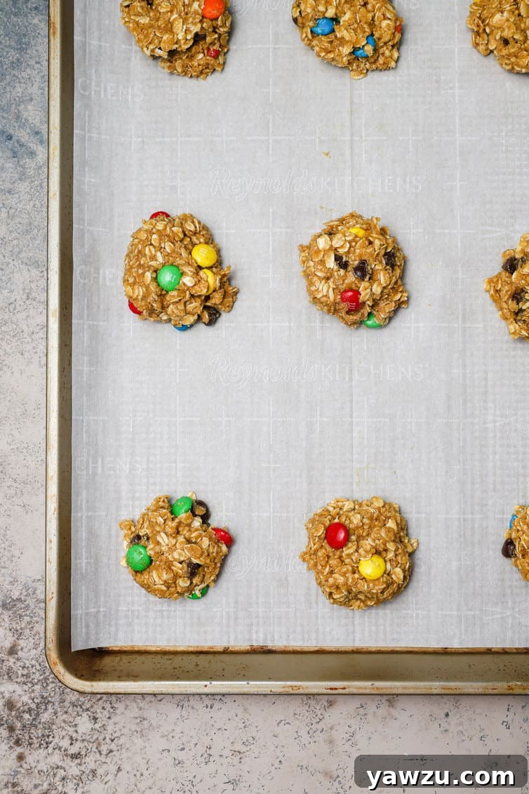 Balls of monster cookie dough on parchment lined baking sheet.