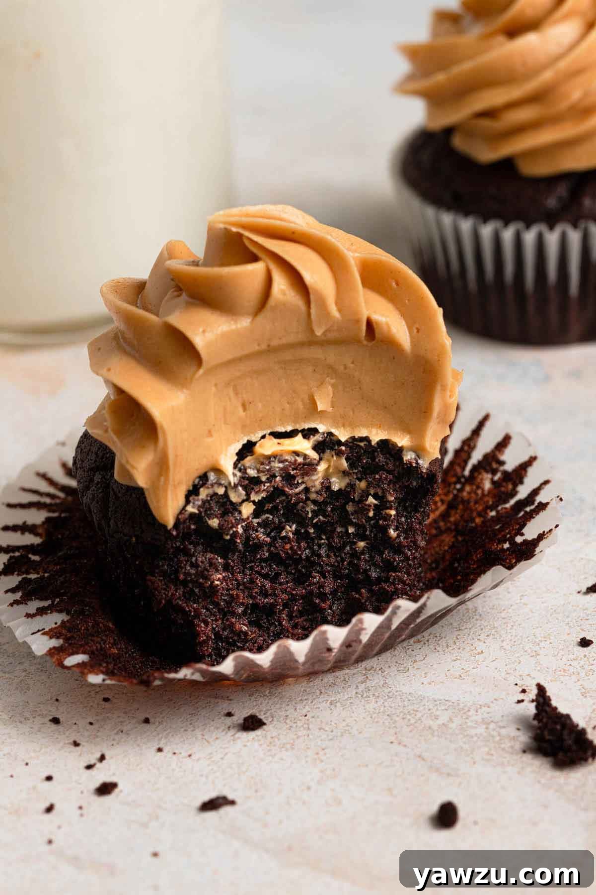 Chocolate cupcake topped with peanut butter frosting, with the wrapped pulled away and the cupcake cut in half.