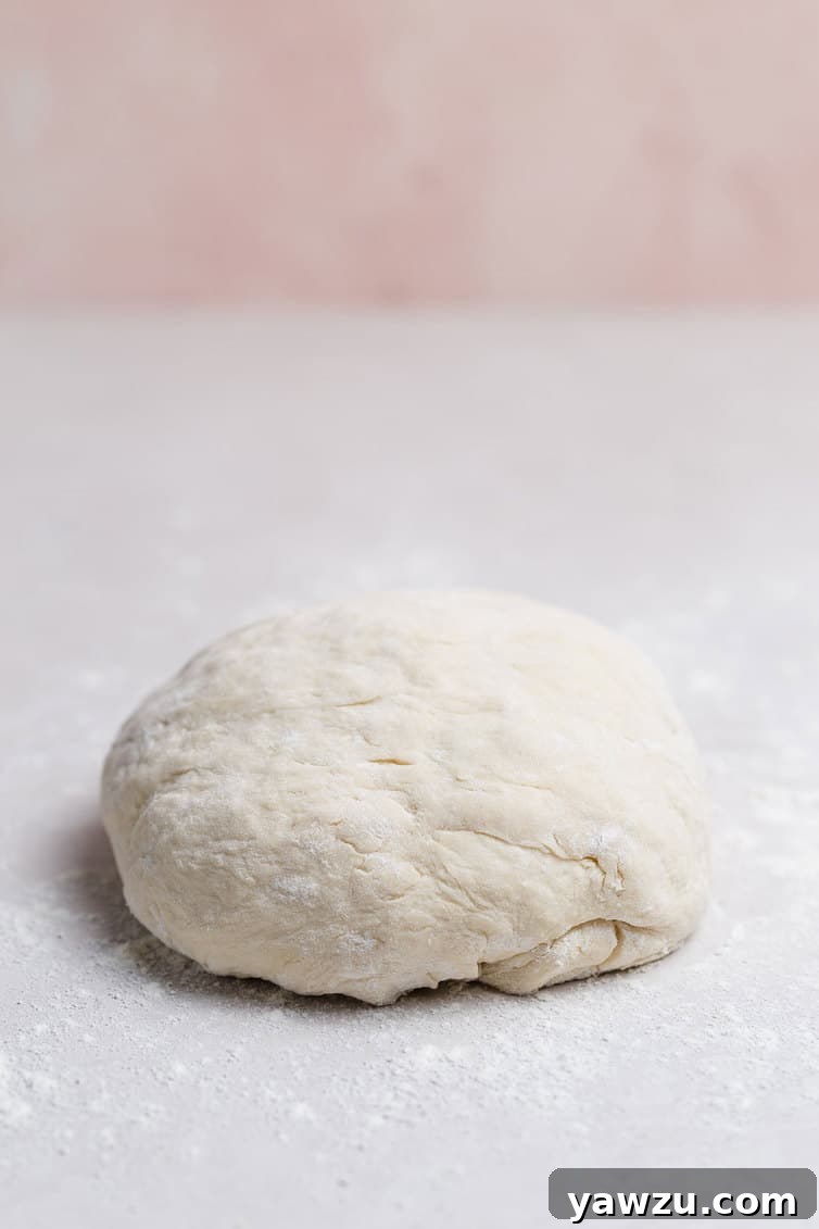 A perfectly formed, smooth ball of homemade pizza dough resting on a lightly floured kitchen counter, ready for its rise.