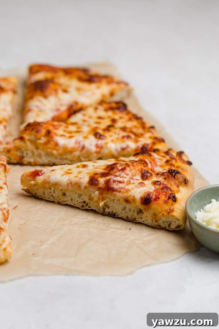 A perfectly baked, triangular slice of cheese pizza resting on a sheet of parchment paper, highlighting its crispy crust and melted cheese.