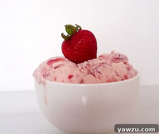 Scoops of vibrant pink strawberry ice cream in a white bowl, garnished with a fresh, ripe strawberry.
