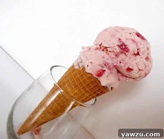 Two generous scoops of homemade strawberry ice cream served in a crispy waffle cone, presented in a glass.