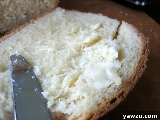 A hand spreading a generous amount of butter onto a freshly sliced piece of homemade American sandwich bread.