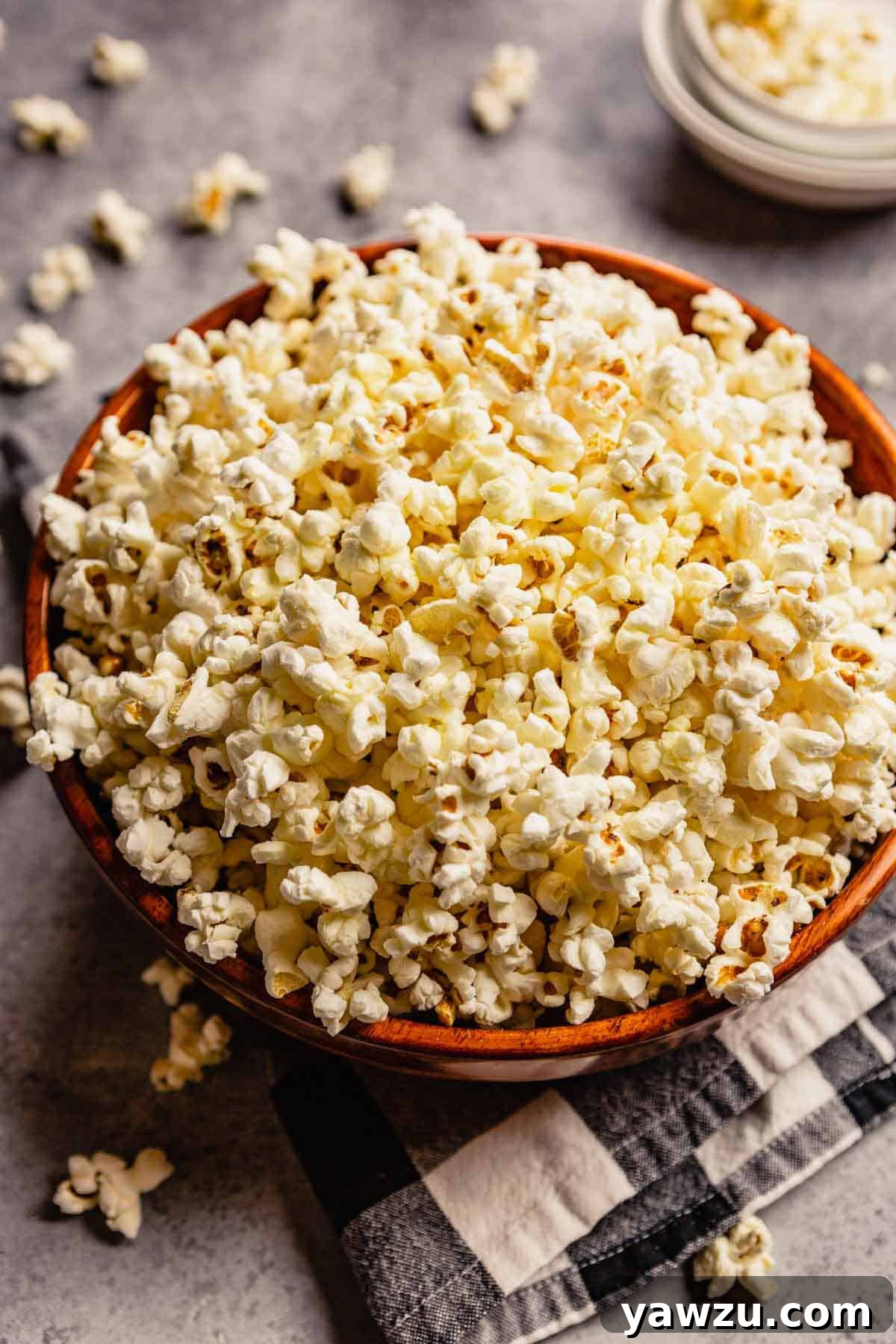 Bowl full of popped popcorn on top of white and black checked towel.