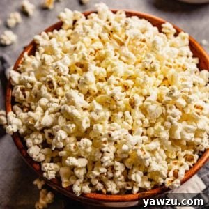 A brown bowl with fresh, homemade popcorn and some pieces of popcorn scattered on the counter.