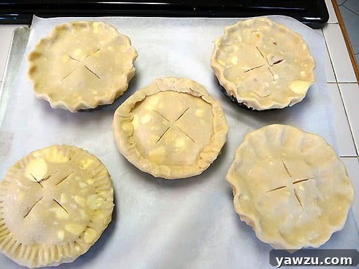 Five unbaked peach pie tartlets arranged neatly on a parchment paper-lined baking sheet, ready for the oven.