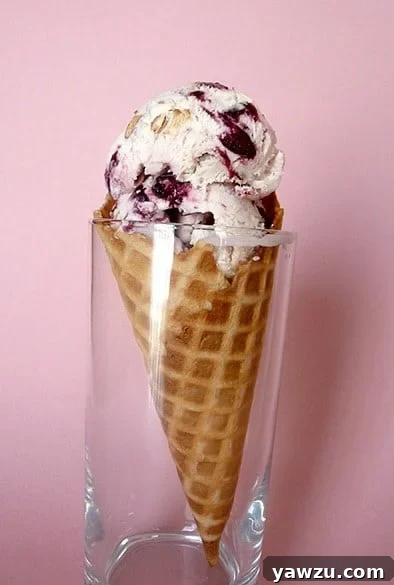 Scoops of toasted almond and candied cherry ice cream in a waffle cone in a glass, a gourmet dessert.