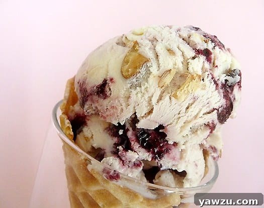 Close up image of scoops of toasted almond and candied cherry ice cream in a waffle cone, highlighting the textures.