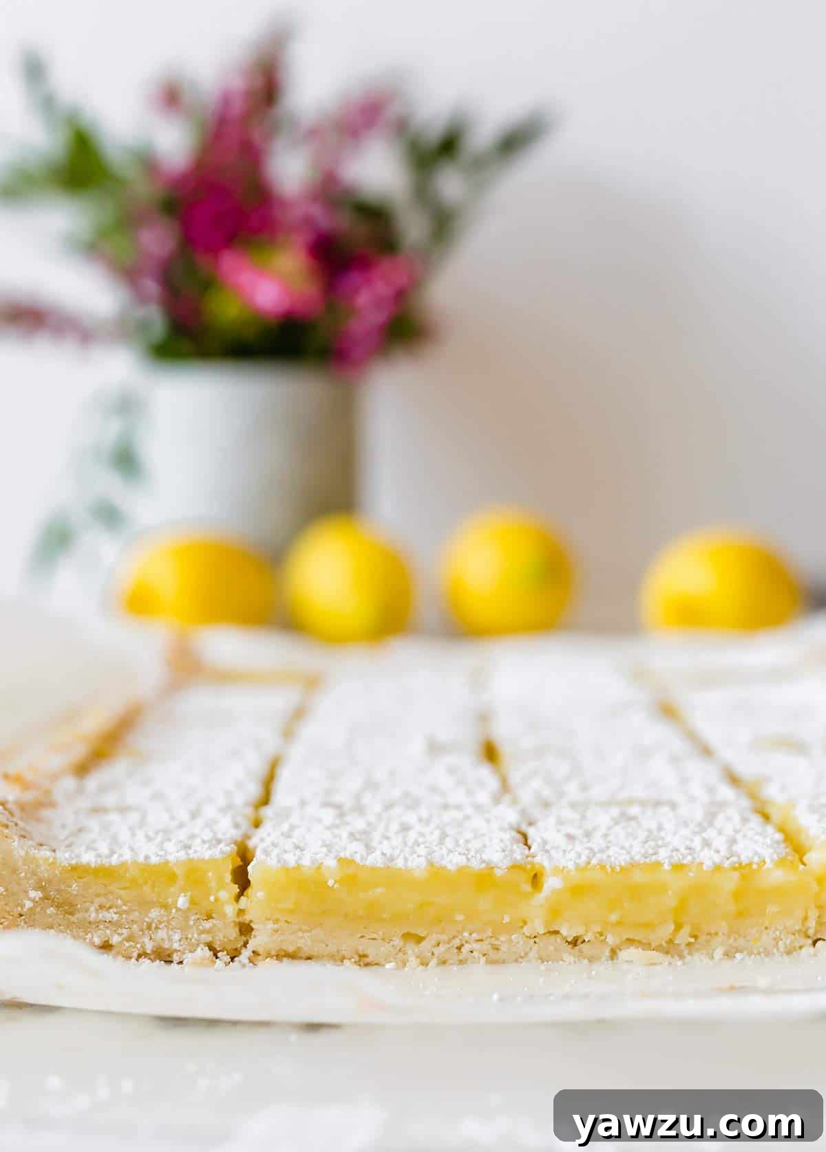 Freshly baked lemon bars neatly sliced into perfect squares, resting on a sheet of parchment paper, ready to be served or dusted with sugar.