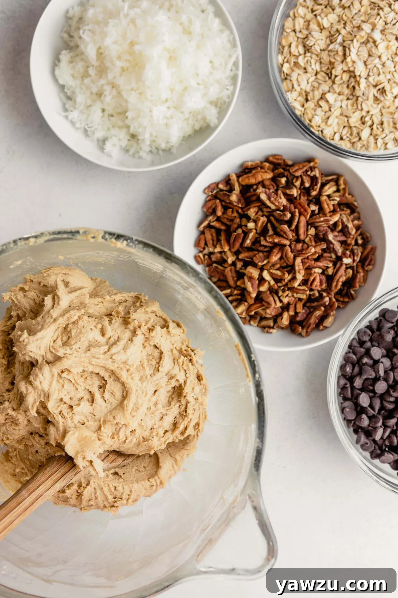 Cookie dough in a glass bowl with mix-ins in prepped bowls next to it.