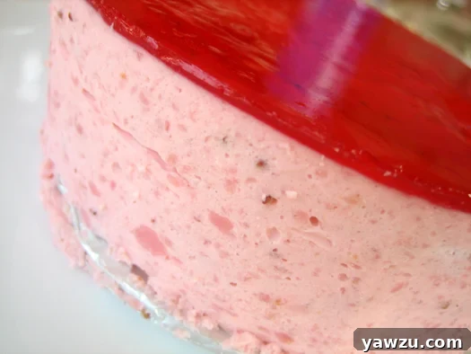 Side view of a perfectly frosted strawberry mirror cake, showcasing its vibrant red glaze and elegant layers.