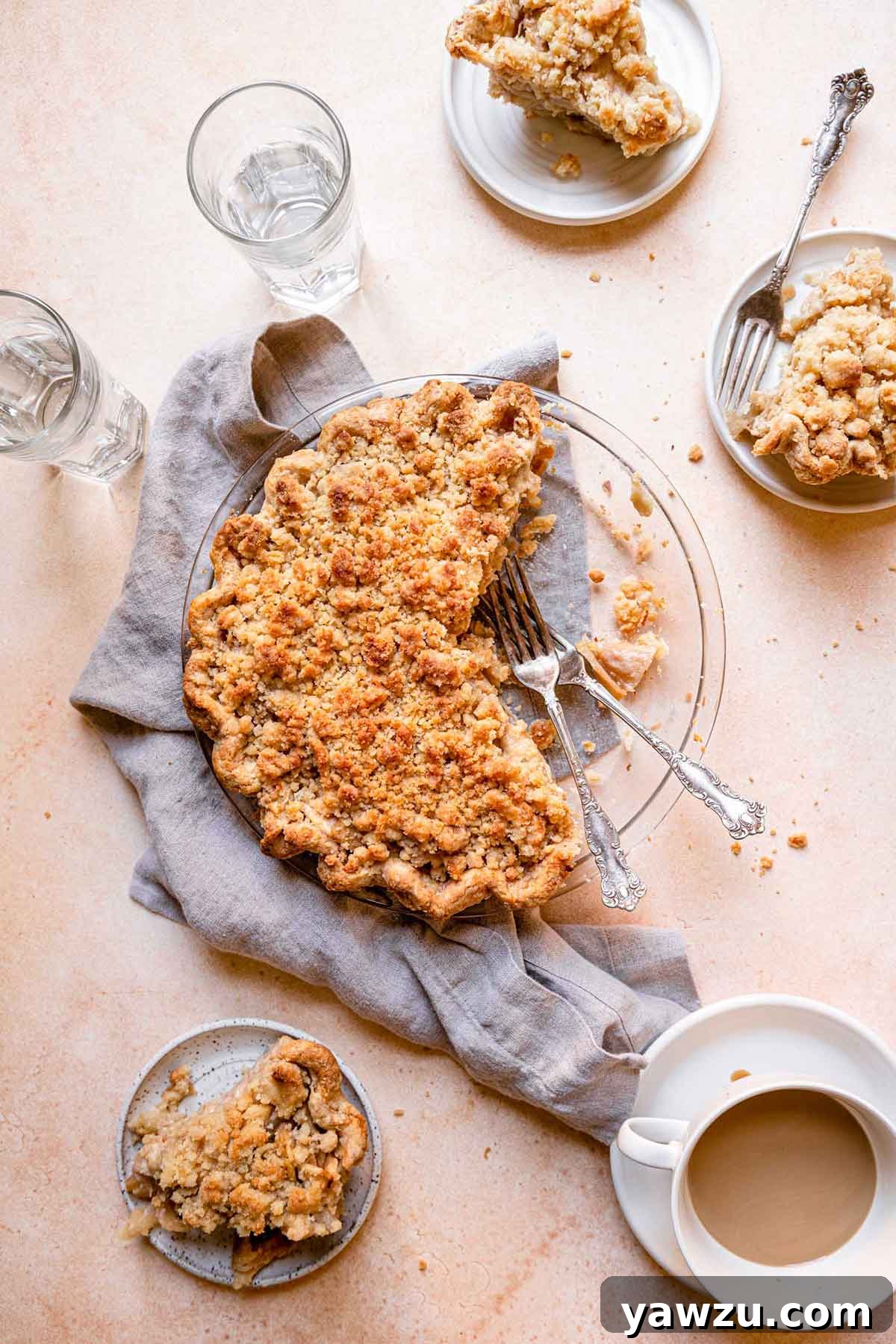 Overhead photo of a Dutch apple pie in a glass pie plate, with several slices already removed and placed on small white dishes in the surrounding area.