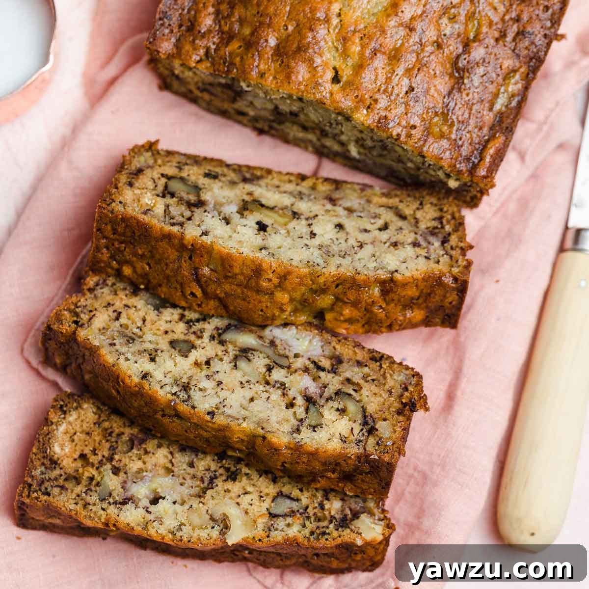 Three perfectly sliced pieces of banana nut bread resting on a pink cloth napkin, with the remaining loaf visible in the background.