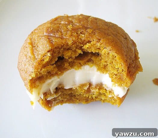 Pumpkin whoopie pie with maple cream cheese filling with a bite taken from it on a white plate.