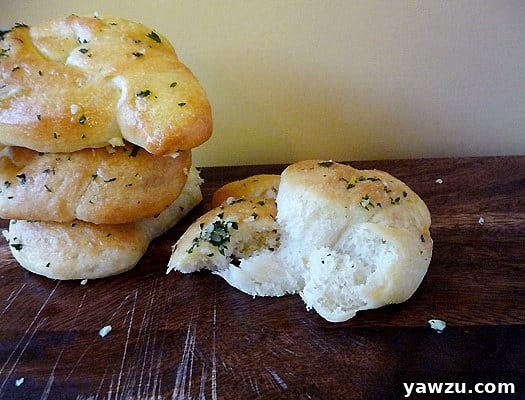 A close-up shot of a stack of three garlic knots with a fourth knot on the counter with a bite taken from it.