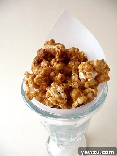 Homemade Cracker Jack popcorn served in a tall glass, showcasing the caramel coating and peanuts.