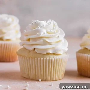 A square image of a vanilla cupcake with vanilla frosting with another in the back left and one to the right.