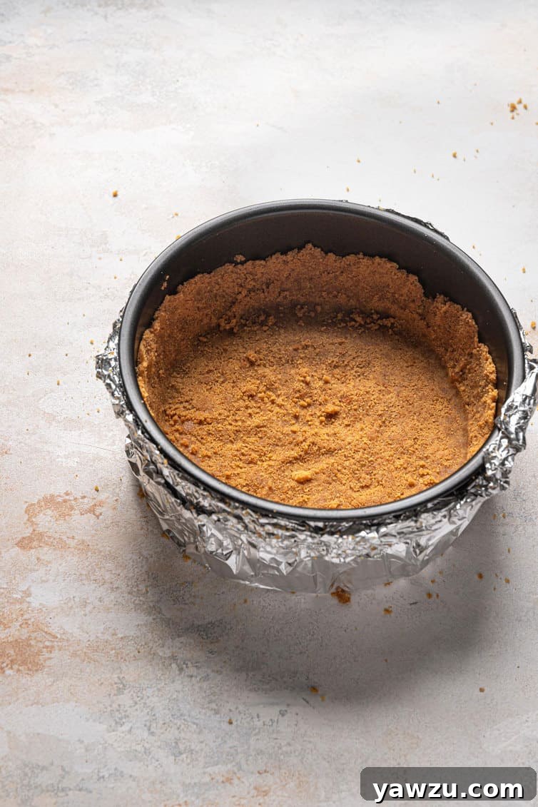 A 9-inch springform pan, meticulously lined with the baked gingersnap crust, sits ready for the cheesecake filling.