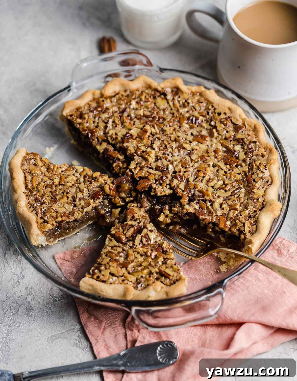 Glass pie plate with pecan pie, two slices cut but still in pie plate with a fork.