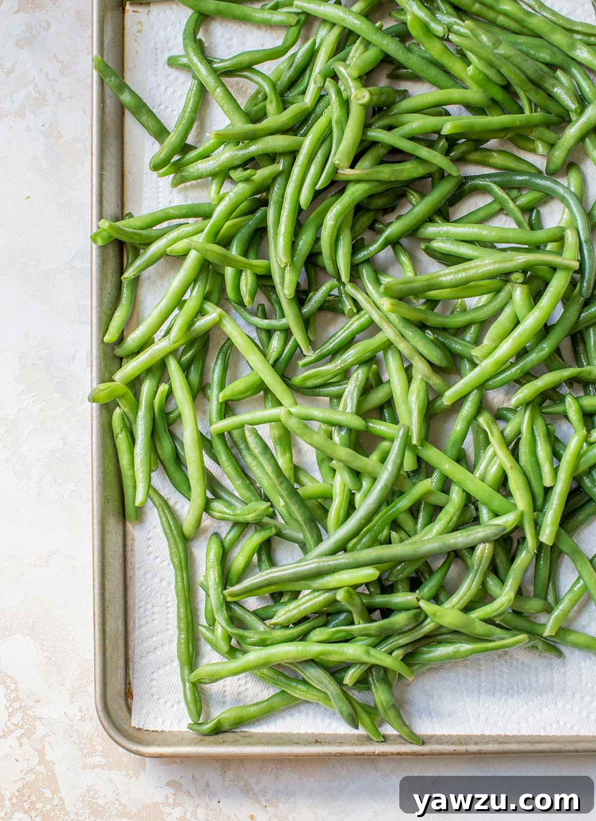 Photo of vibrant fresh green beans spread out on a paper towel-lined baking sheet, ready for preparation.