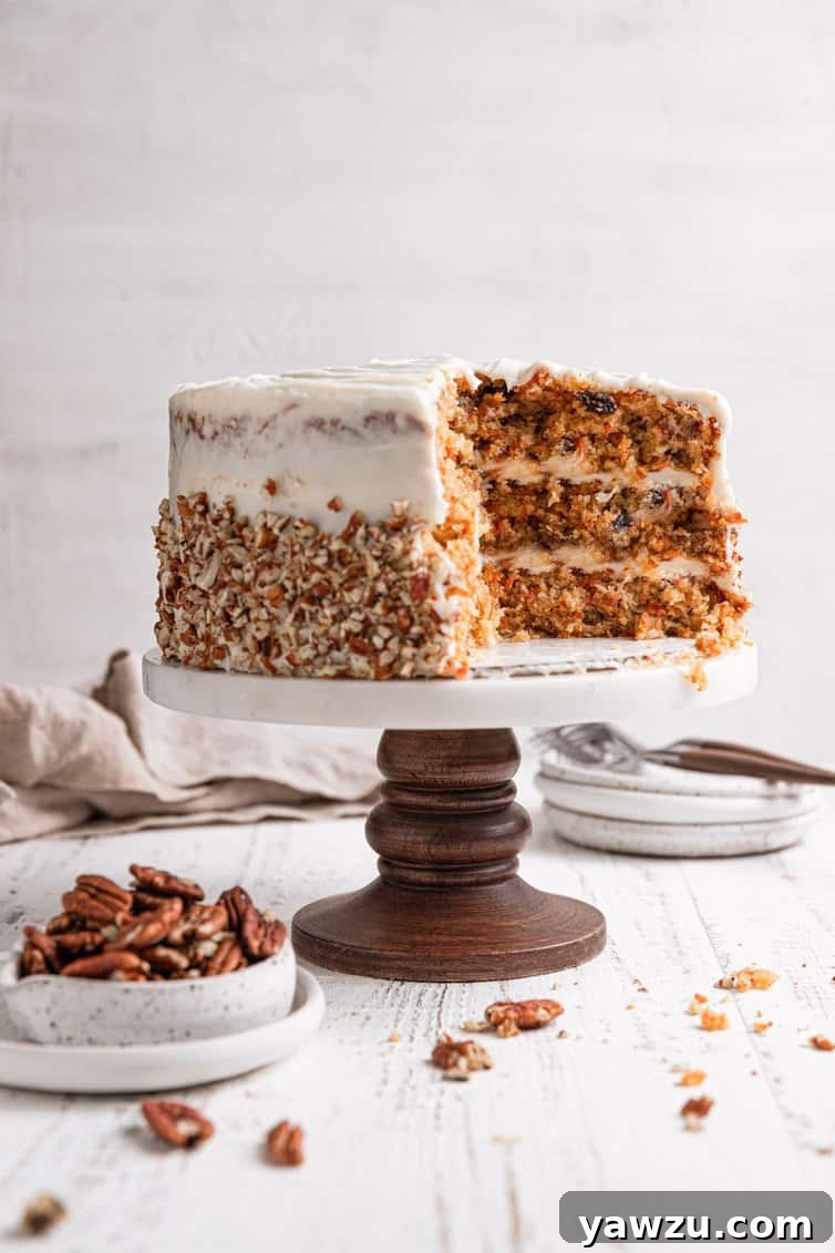 Carrot cake on a cake pedestal, showing the inside of the cake with layers of frosting and add-ins.