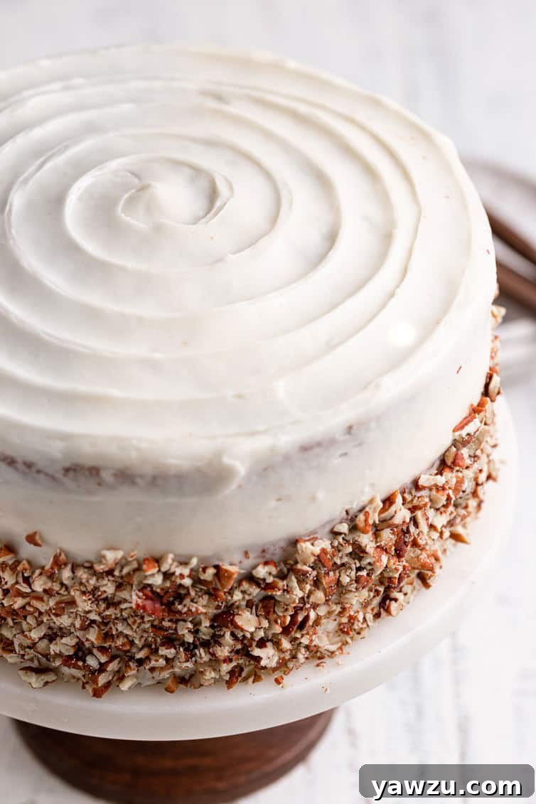 Fully assembled carrot cake with spiral icing design on top and chopped pecans pressed into its sides.