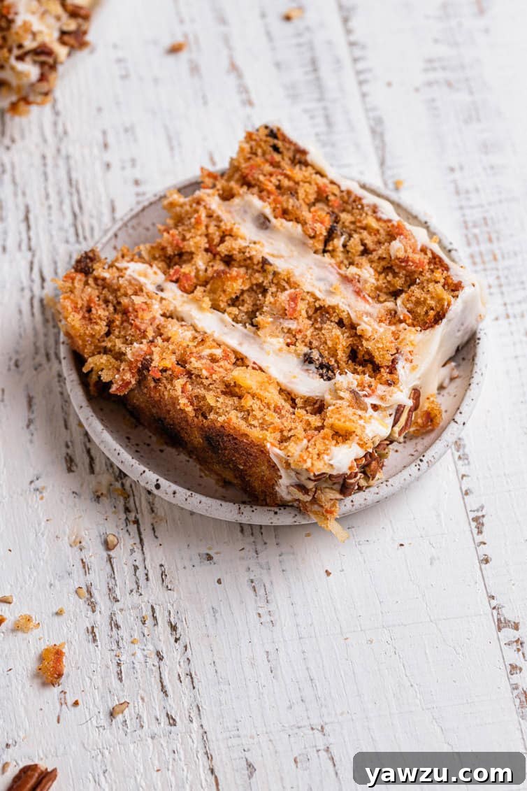 A slice of moist carrot cake lying on its side on a white plate, showing the rich texture and inclusions.
