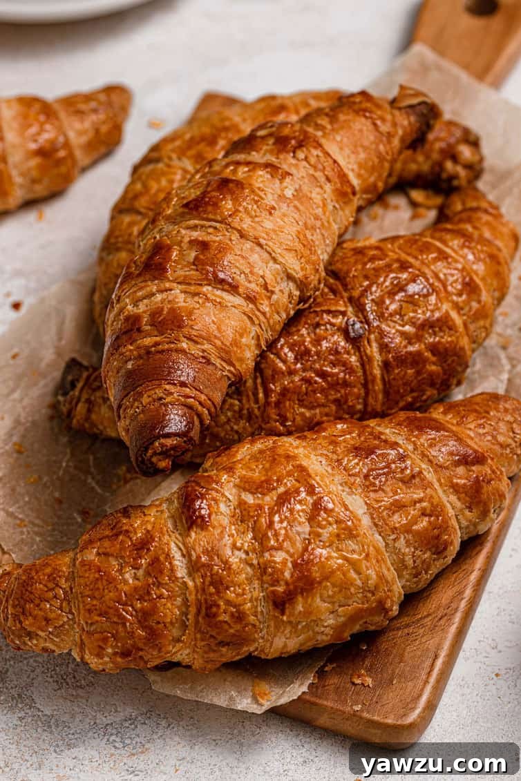 A delectable stack of perfectly baked homemade croissants, golden and inviting, artfully arranged on a rustic wooden cutting board, emphasizing their fresh appeal.